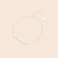 Delicate rhodium-plated silver chain bracelet with row of small baroque pearls centered on white background.