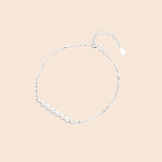 Delicate rhodium-plated silver chain bracelet with row of small baroque pearls centered on white background.