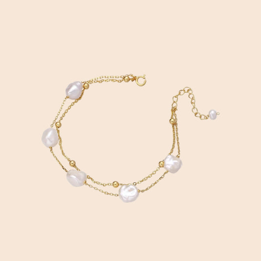 Double-strand gold bracelet with irregular baroque pearls and smooth freshwater pearls on cream background.