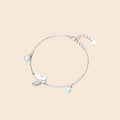 Delicate rhodium-plated silver chain bracelet with butterfly charm and two freshwater pearls on cream background