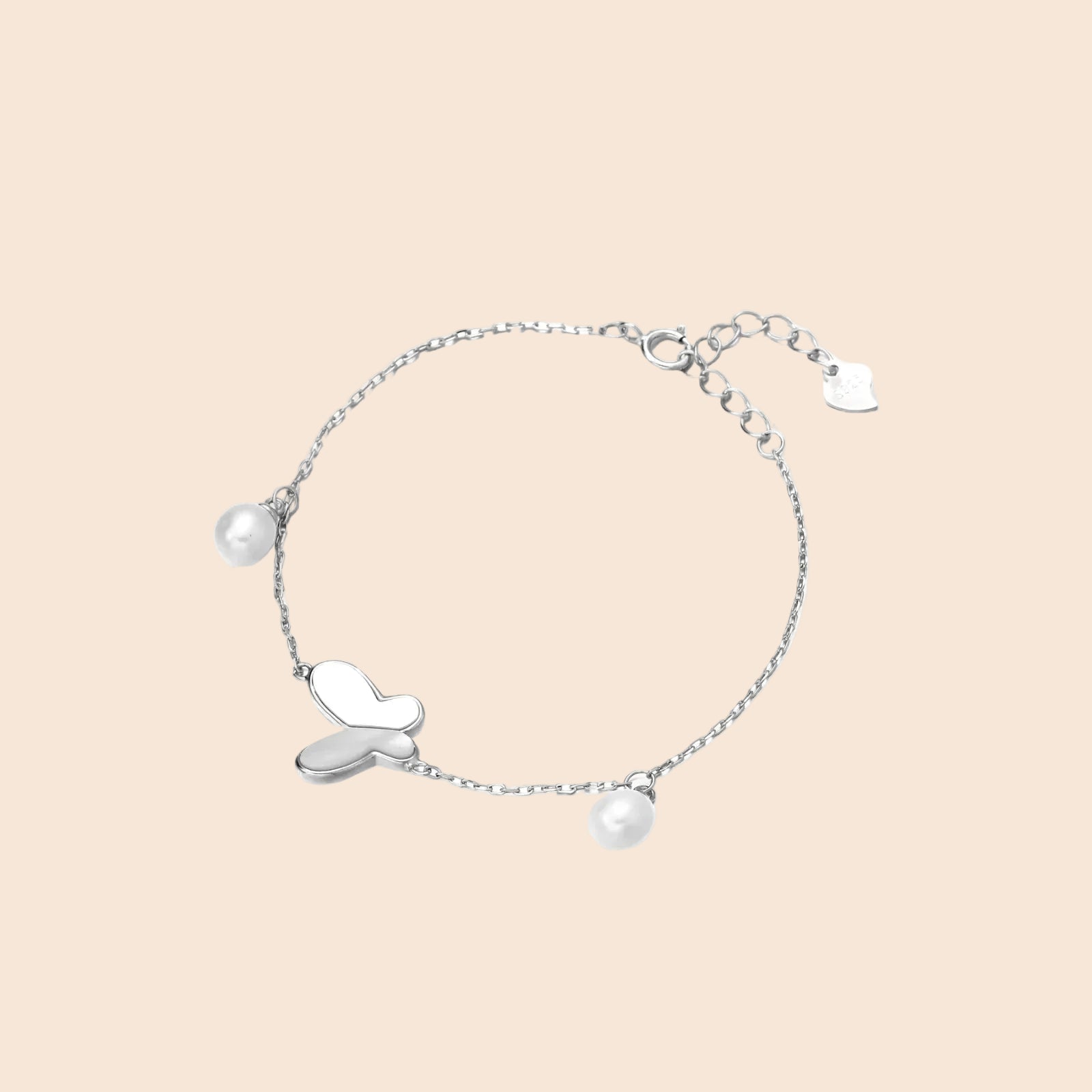 Delicate rhodium-plated silver chain bracelet with butterfly charm and two freshwater pearls on cream background