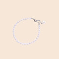 Delicate freshwater pearl bracelet with rhodium-plated silver clasp and single pearl drop charm on cream background