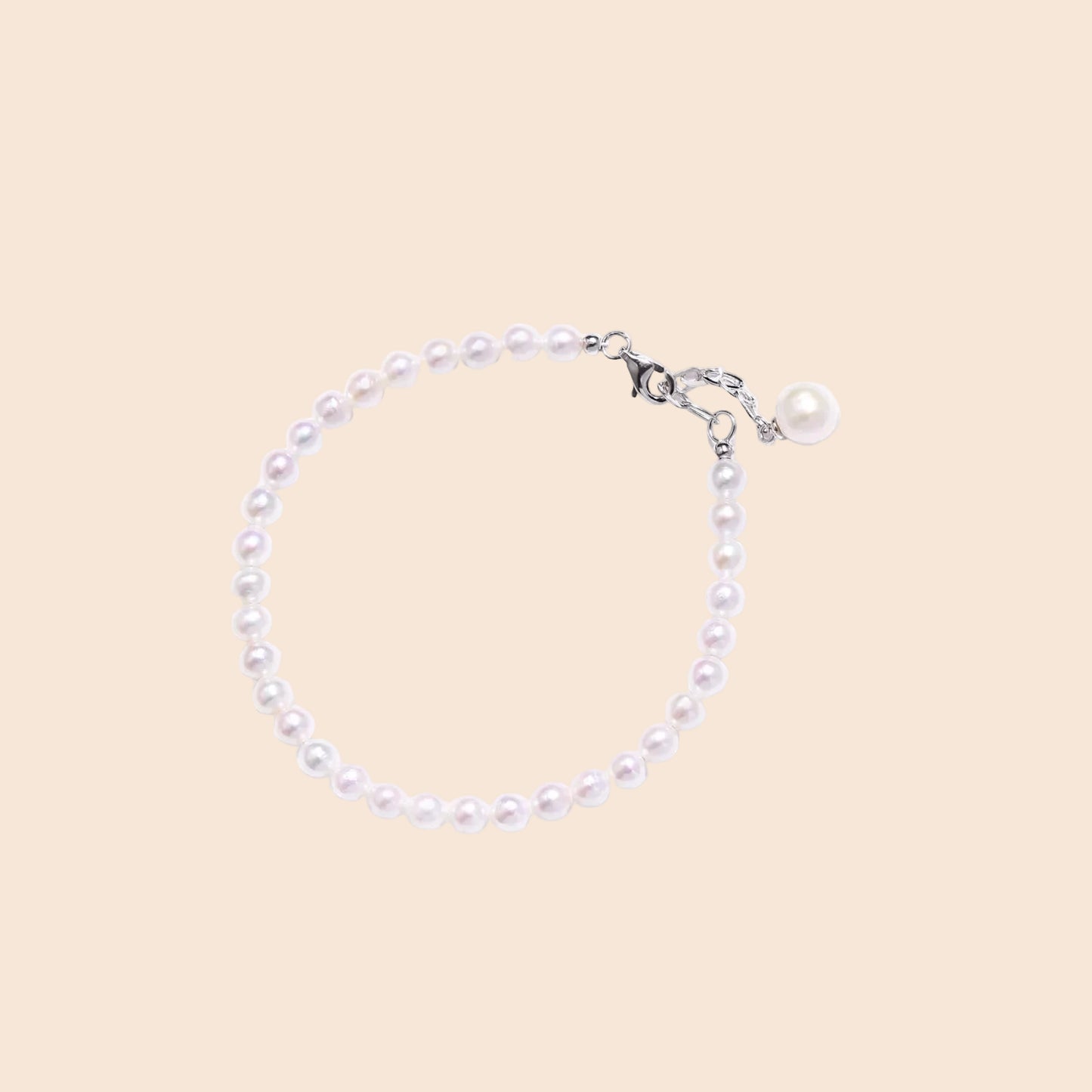 Delicate freshwater pearl bracelet with rhodium-plated silver clasp and single pearl drop charm on cream background