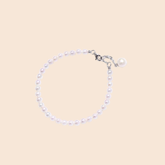 Delicate freshwater pearl bracelet with rhodium-plated silver clasp and single pearl drop charm on cream background