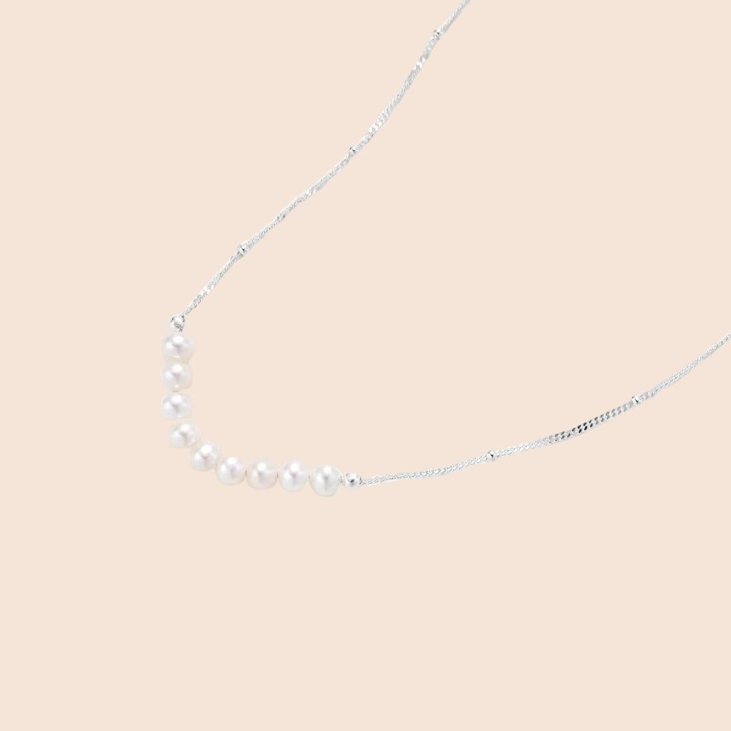 Delicate sterling silver chain necklace with small freshwater pearls arranged in a curved smile arc on cream background.