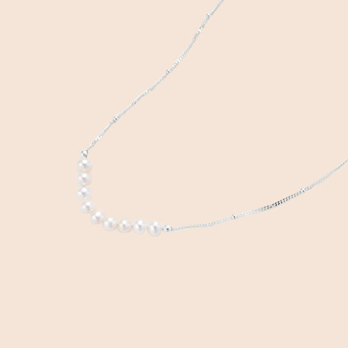 Delicate sterling silver chain necklace with small freshwater pearls arranged in a curved smile arc on cream background.