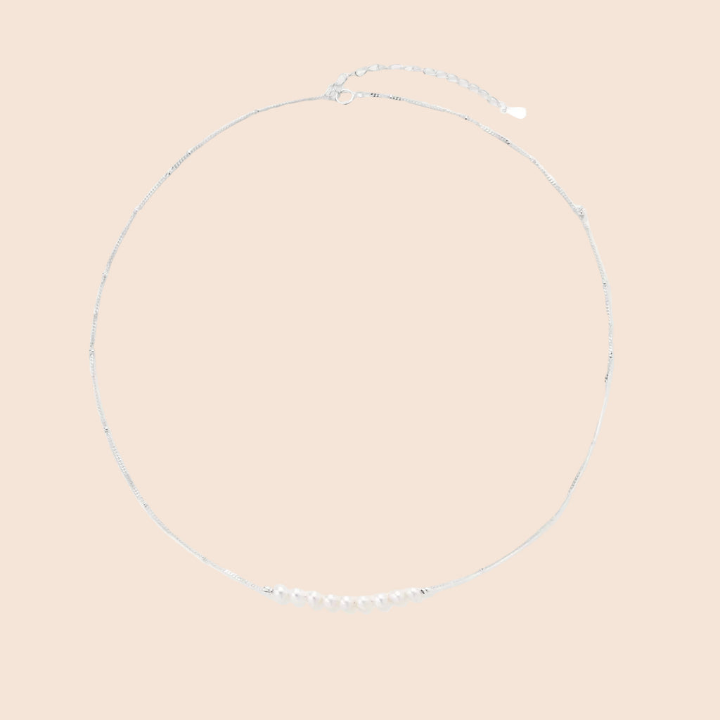 Delicate sterling silver chain necklace with small freshwater pearls arranged in a curved smile arc on cream background.