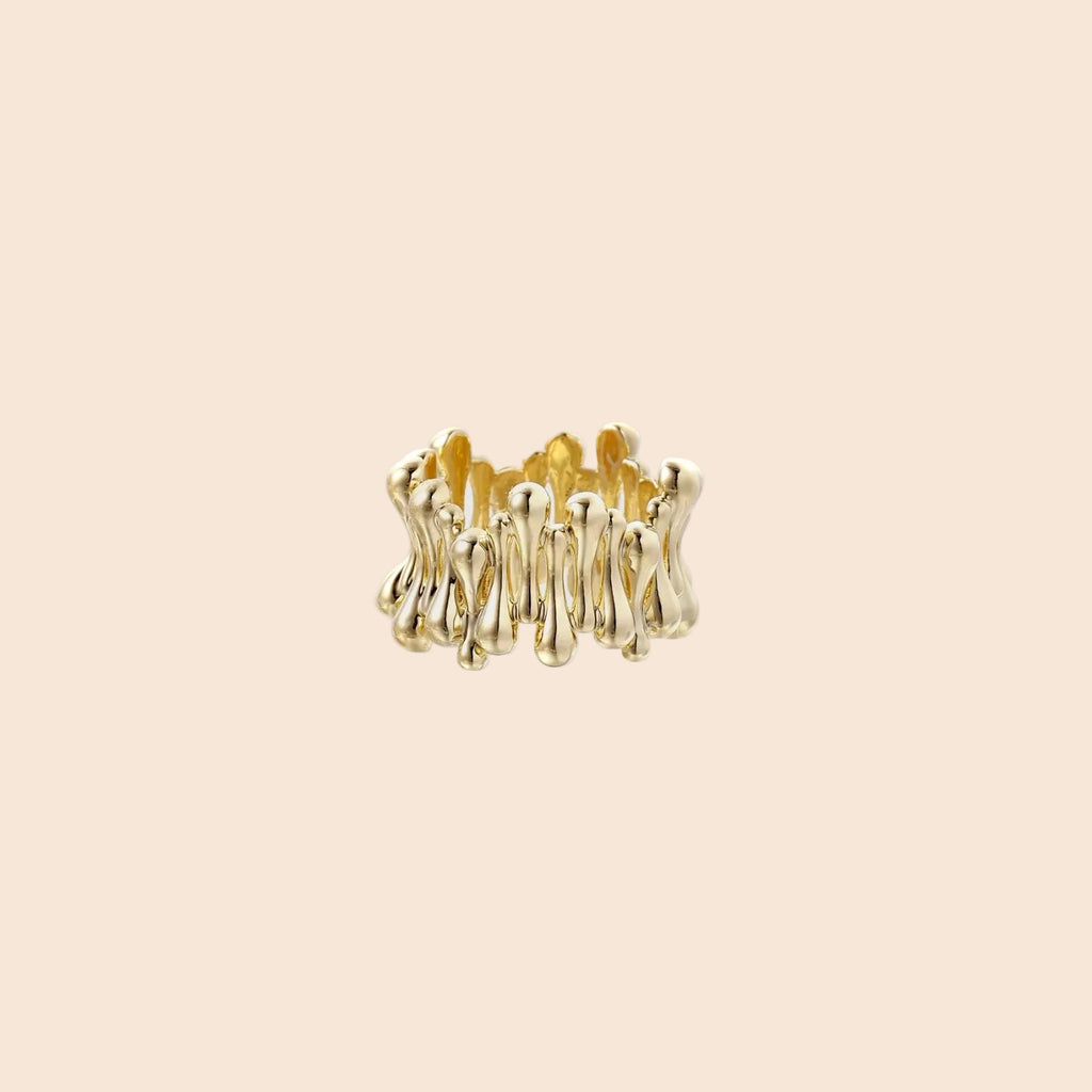 Gold-plated brass ring with sculptural petal-like elements in a wide band design on beige background