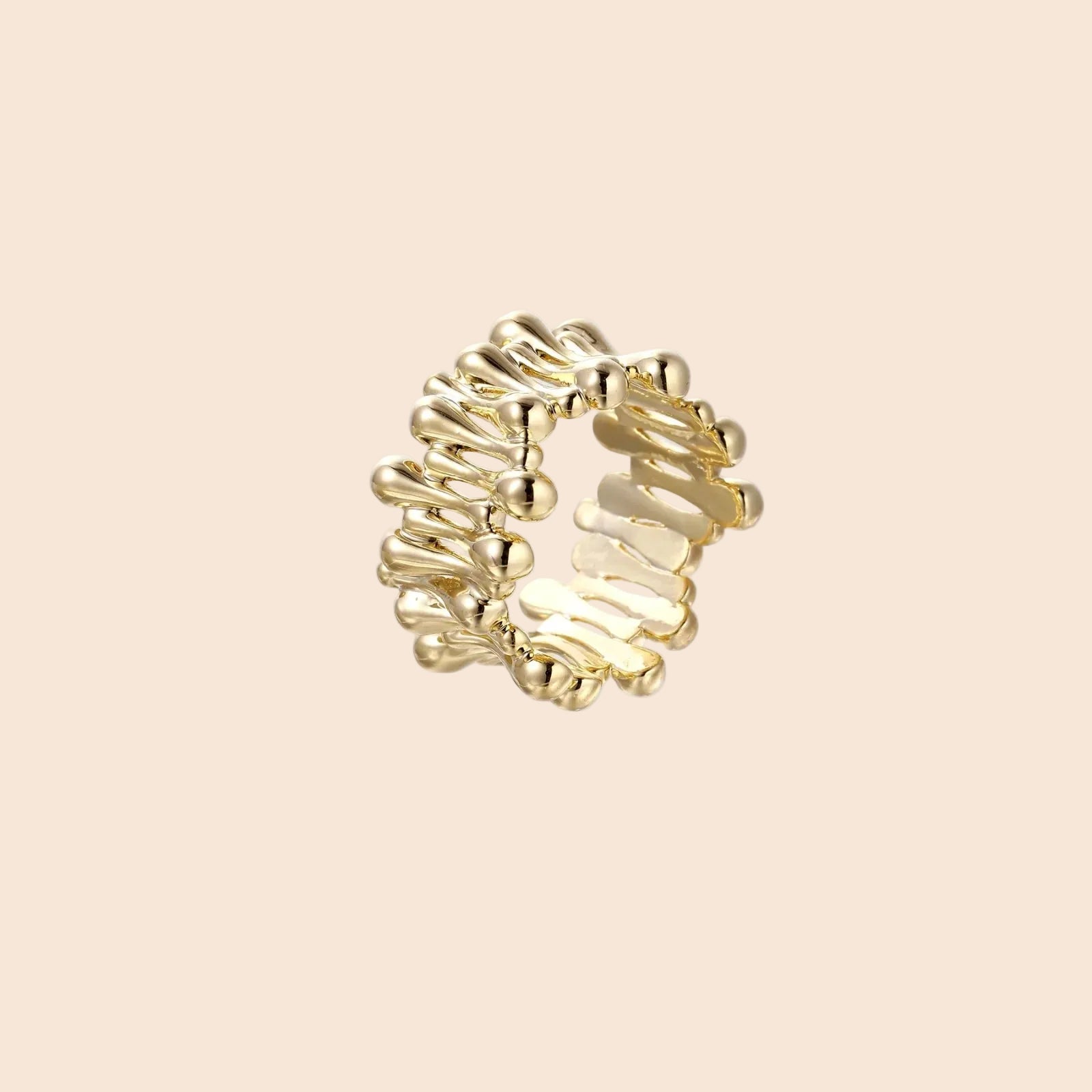 Gold-plated brass ring with sculptural petal-like elements in a wide band design on beige background