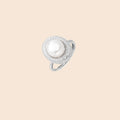 Silver ring with lustrous white pearl center surrounded by sparkling crystal halo on light background.