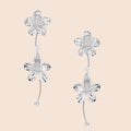 Silver-white asymmetric earrings with textured flower petals and crystal centers on cream background