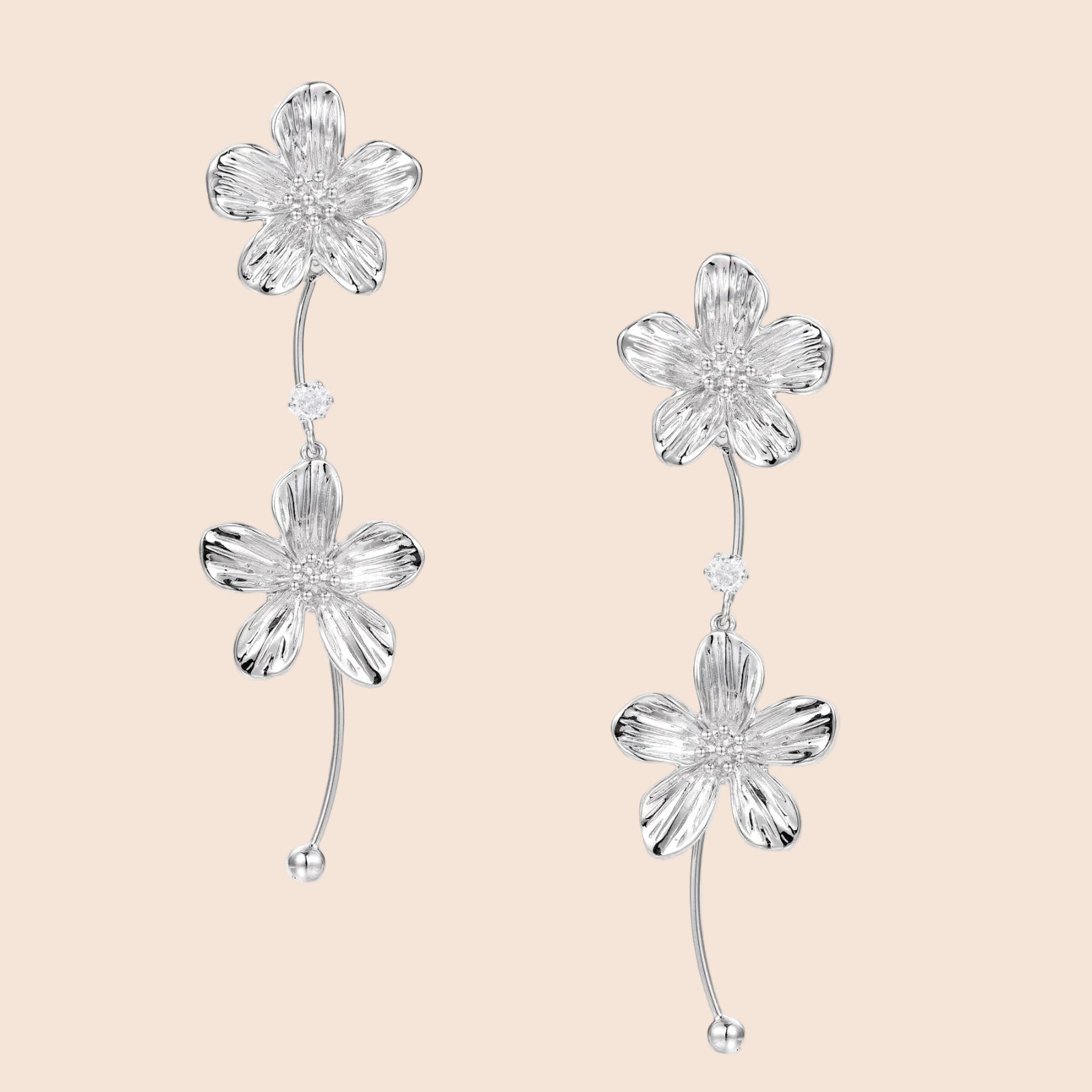 Silver-white asymmetric earrings with textured flower petals and crystal centers on cream background