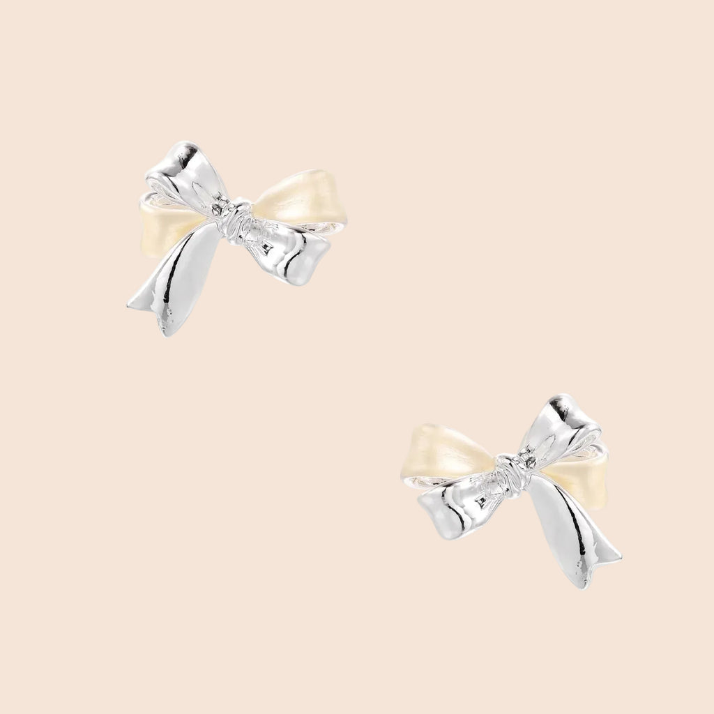Dimensional bow stud earrings in white gold plated brass with silver and cream two-tone finish on neutral background