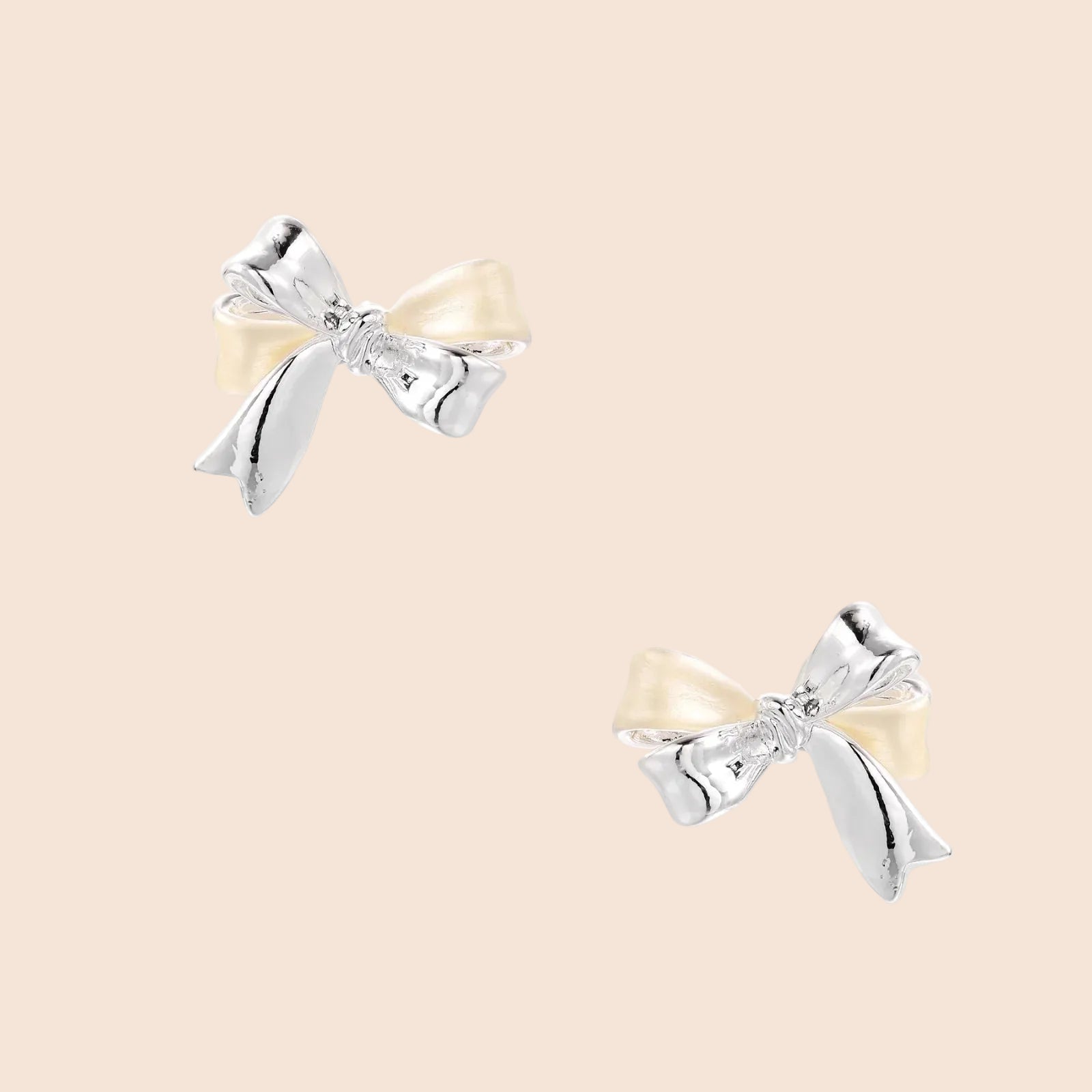 Dimensional bow stud earrings in white gold plated brass with silver and cream two-tone finish on neutral background