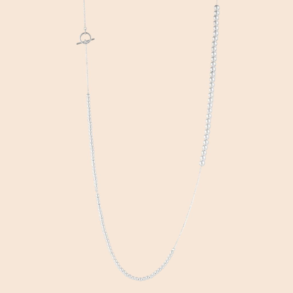 Long sterling silver beaded necklace with graduated sphere design, toggle clasp, and delicate chain extension on white background