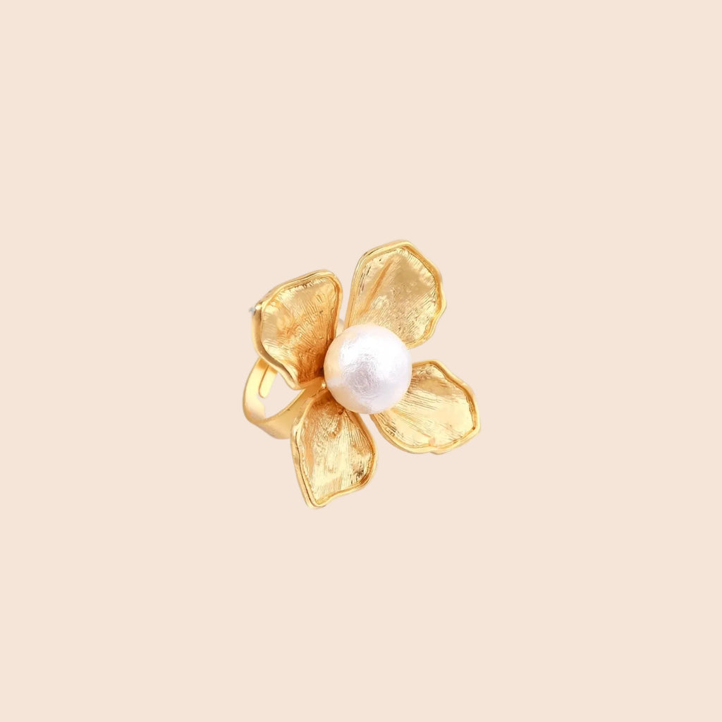 Gold-plated flower ring with textured petals and white cotton pearl center on cream background
