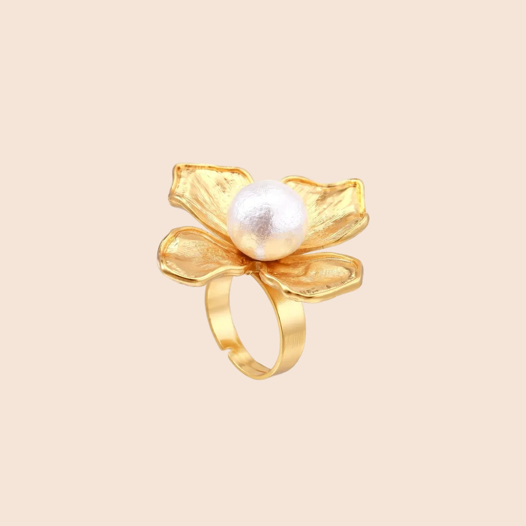 Gold-plated flower ring with textured petals and white cotton pearl center on cream background