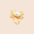 Gold-plated flower ring with textured petals and white cotton pearl center on cream background