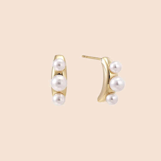 14K gold-plated curved stud earrings with three white freshwater pearls aligned vertically on cream background