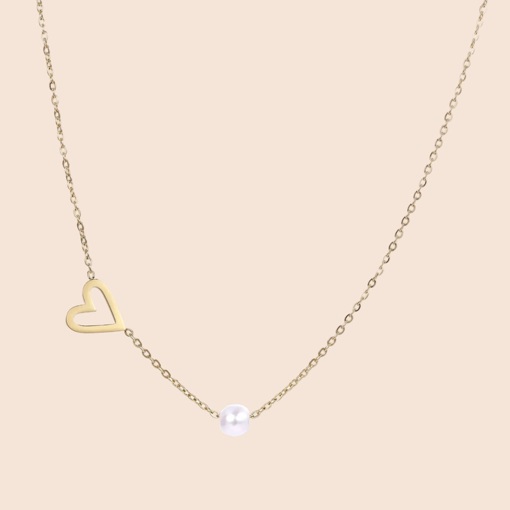 Delicate gold necklace with open heart charm and white pearl bead on fine chain against cream background