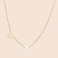 Delicate gold necklace with open heart charm and white pearl bead on fine chain against cream background