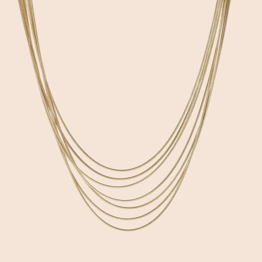 Seven delicate gold-plated snake chains create an elegant layered necklace on a neutral background.