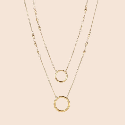 Layered gold necklace set with two open circle pendants and mixed chain styles on beige background