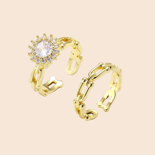 Two adjustable gold rings: chain-link band and halo-style ring with cubic zirconia stones on cream background