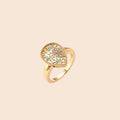 Teardrop-shaped gold-plated ring with turquoise enamel flowers and crystal pavé detail on cream background