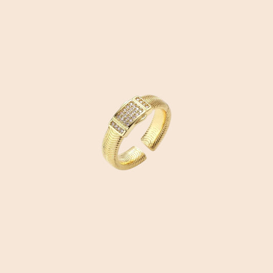 Gold-plated adjustable ring with ribbed band and rectangular pavé cubic zirconia panel on white background.