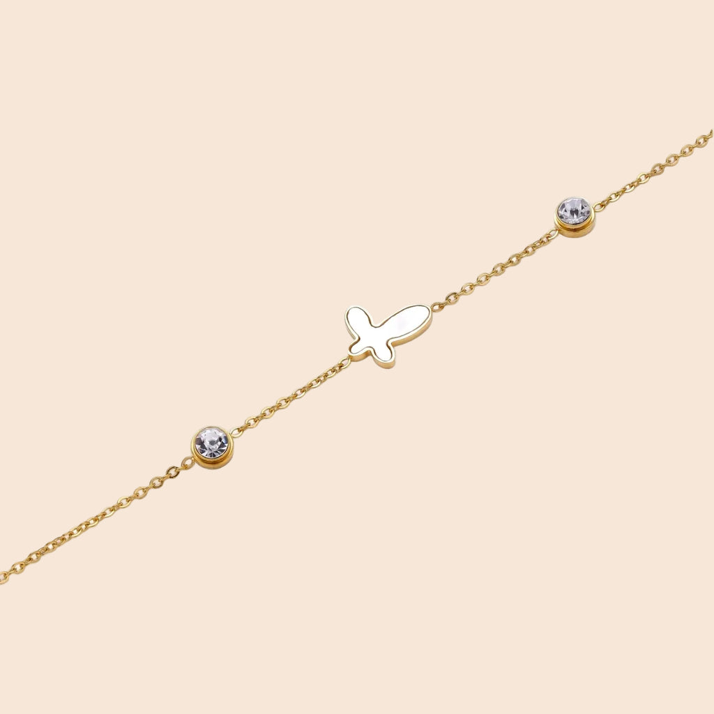 Gold chain bracelet with white mother of pearl butterfly pendant and two bezel-set crystals on cream background