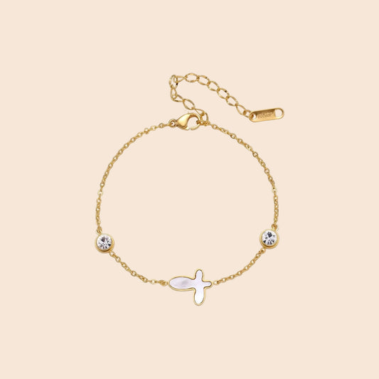 Gold chain bracelet with white mother of pearl butterfly pendant and two bezel-set crystals on cream background