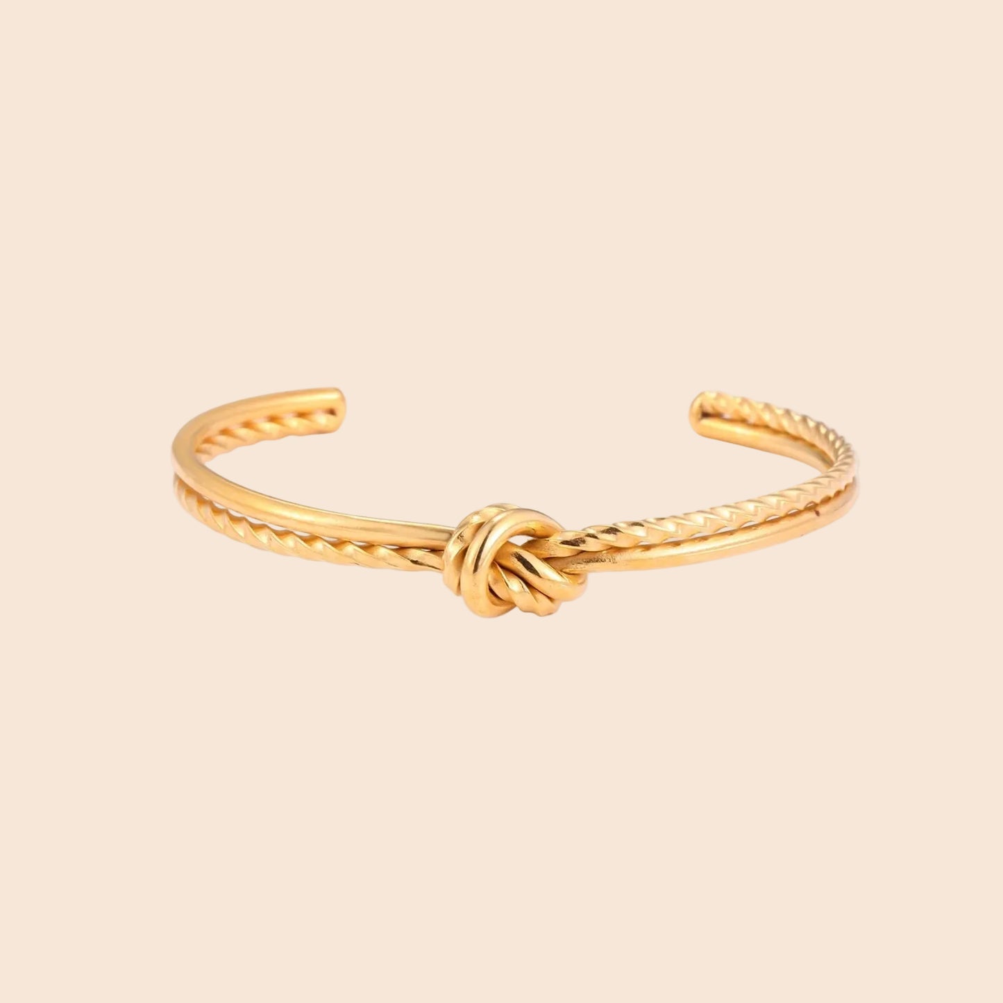 Gold cuff bracelet with twisted rope texture and decorative knot centerpiece on cream background.