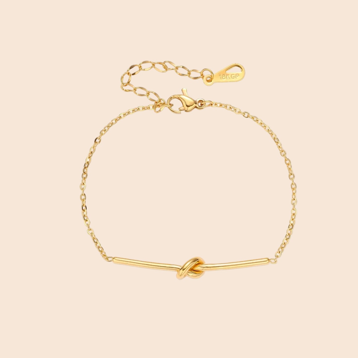 Delicate gold chain bracelet with minimalist bar and centered knot detail on cream background