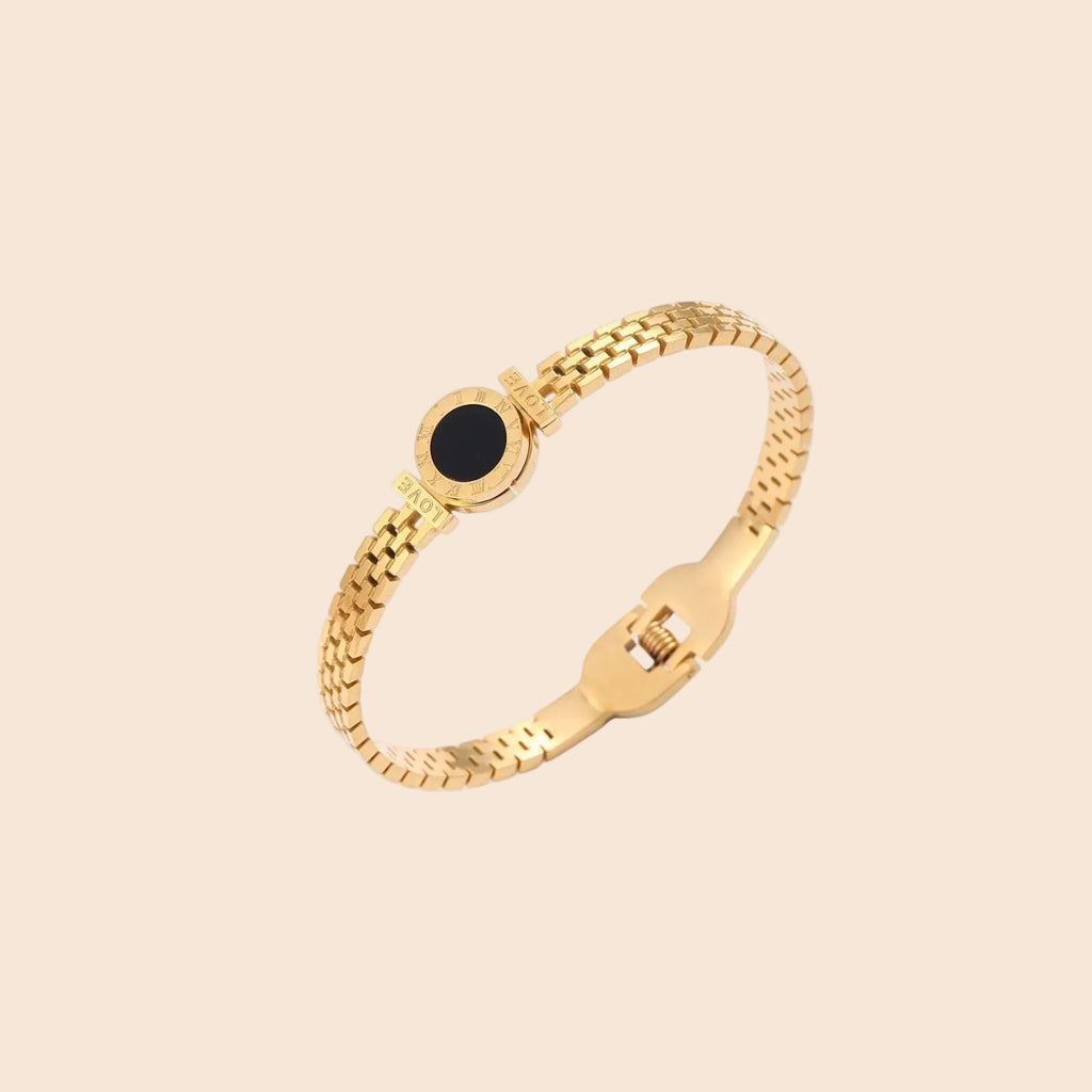 Gold mesh bracelet with circular black mother of pearl medallion featuring Roman numeral engravings and hinged clasp