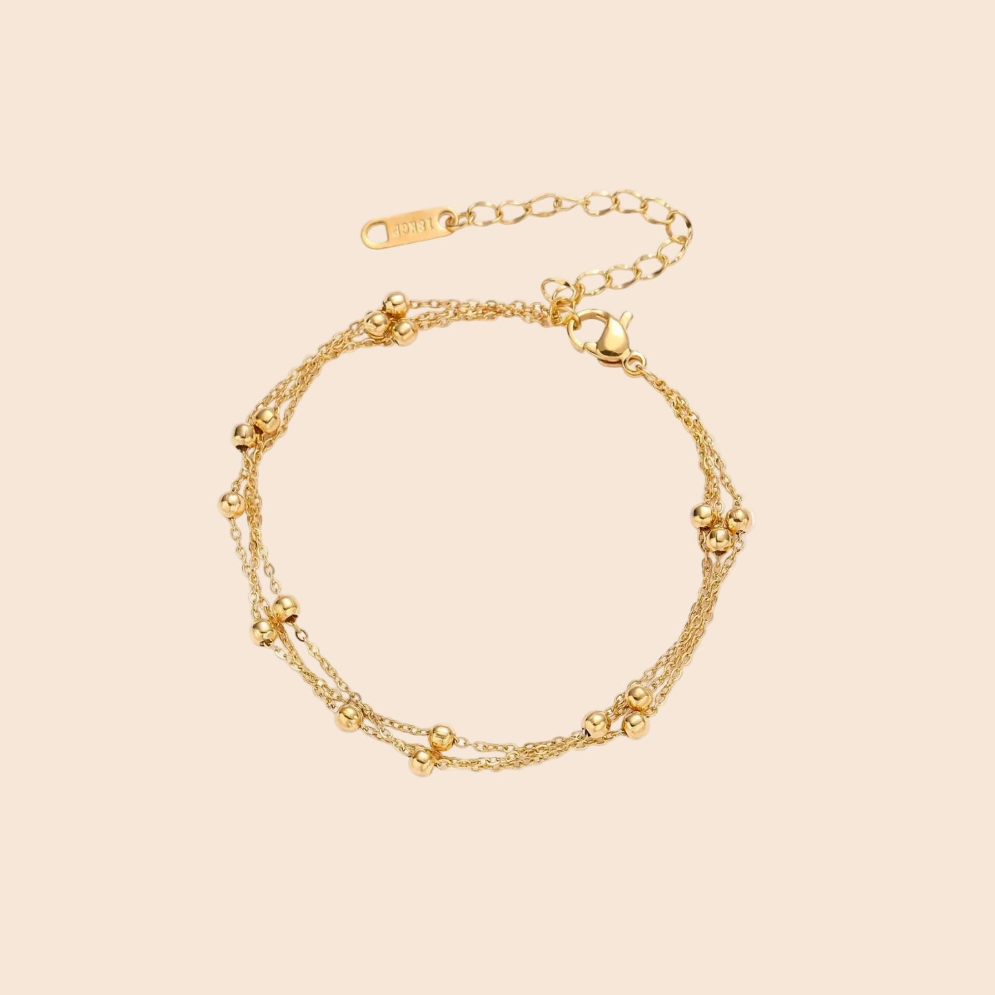Three-strand gold-plated bracelet with clustered ball beads and adjustable clasp on cream background