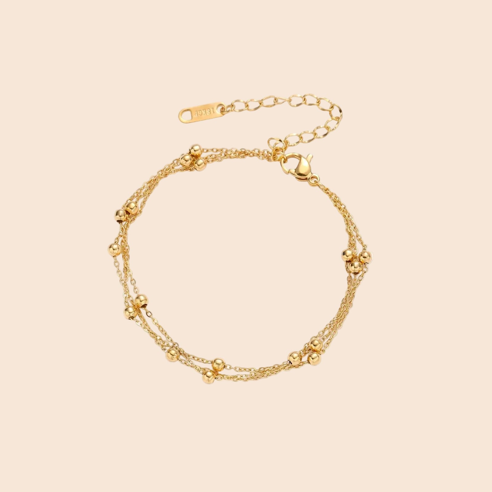 Three-strand gold-plated bracelet with clustered ball beads and adjustable clasp on cream background