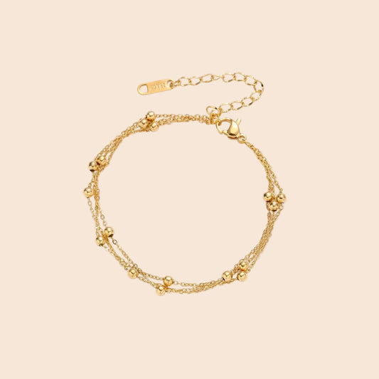Three-strand gold-plated bracelet with clustered ball beads and adjustable clasp on cream background