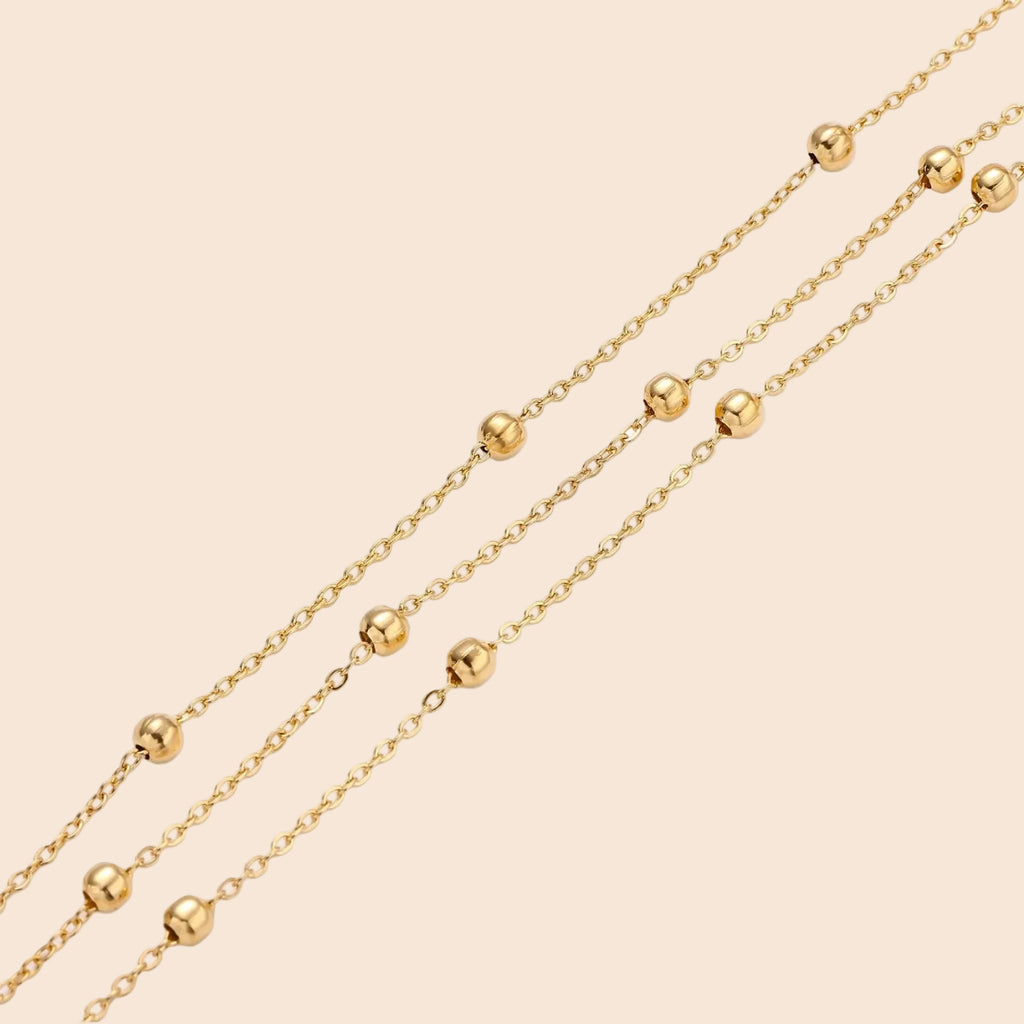 Three-strand gold-plated bracelet with clustered ball beads and adjustable clasp on cream background