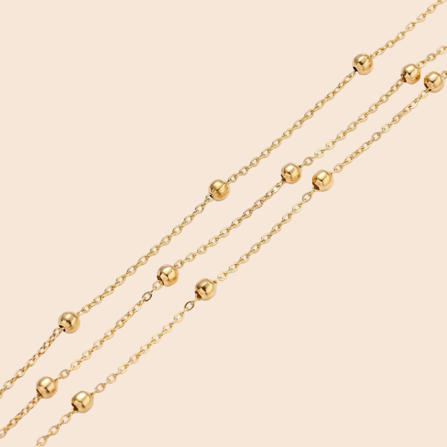 Three-strand gold-plated bracelet with clustered ball beads and adjustable clasp on cream background