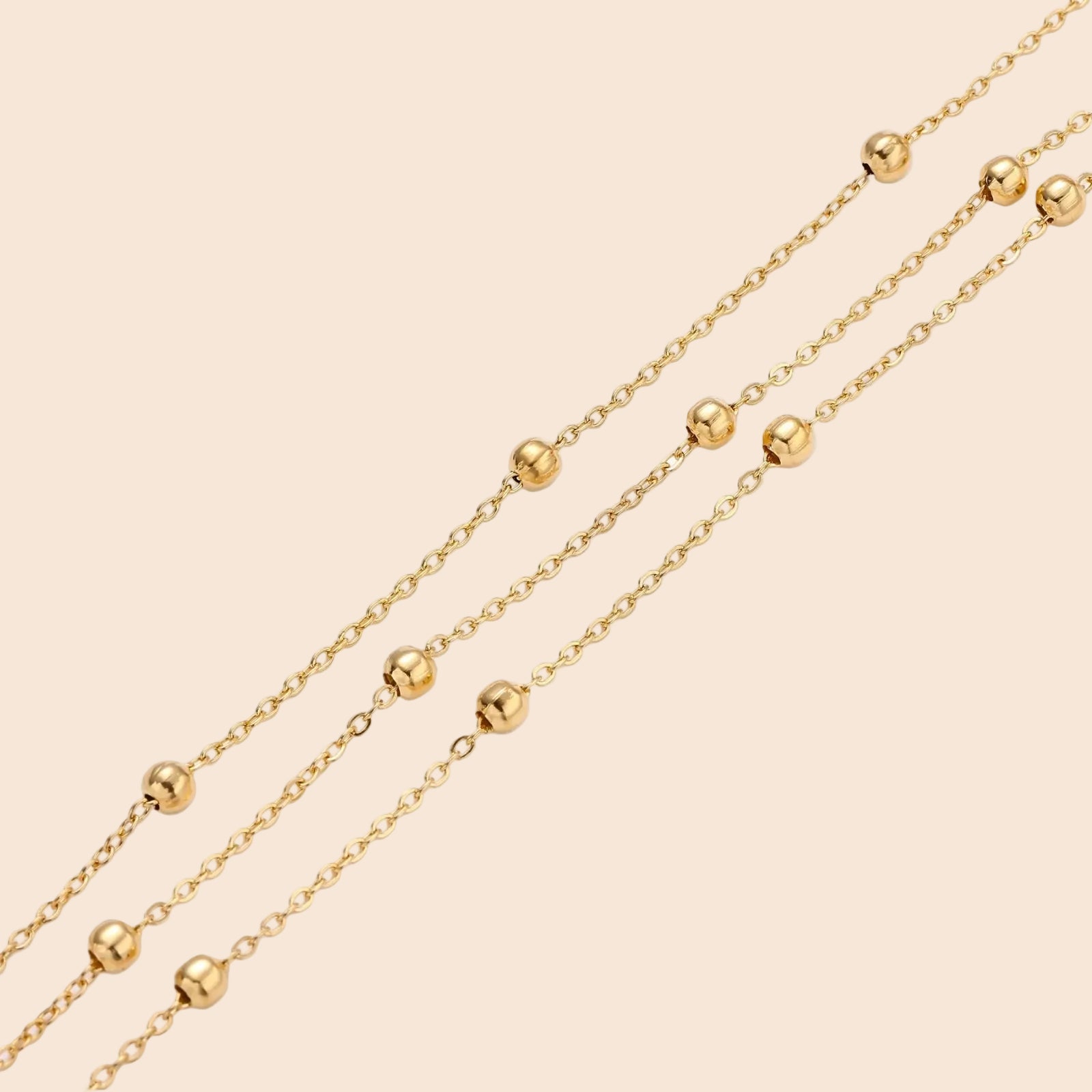 Three-strand gold-plated bracelet with clustered ball beads and adjustable clasp on cream background