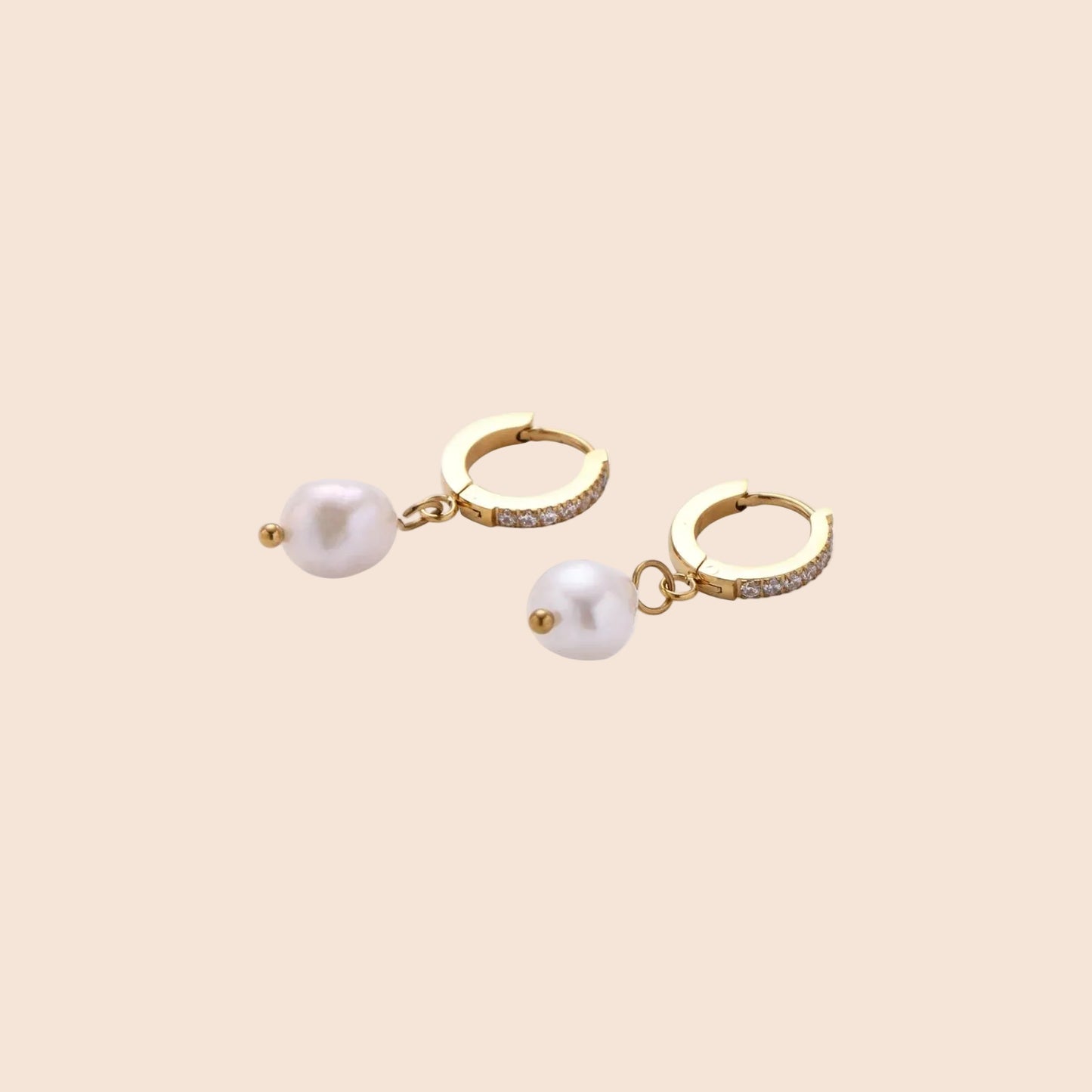 Gold huggie hoop earrings with pavé crystals and white freshwater pearl drops on cream background