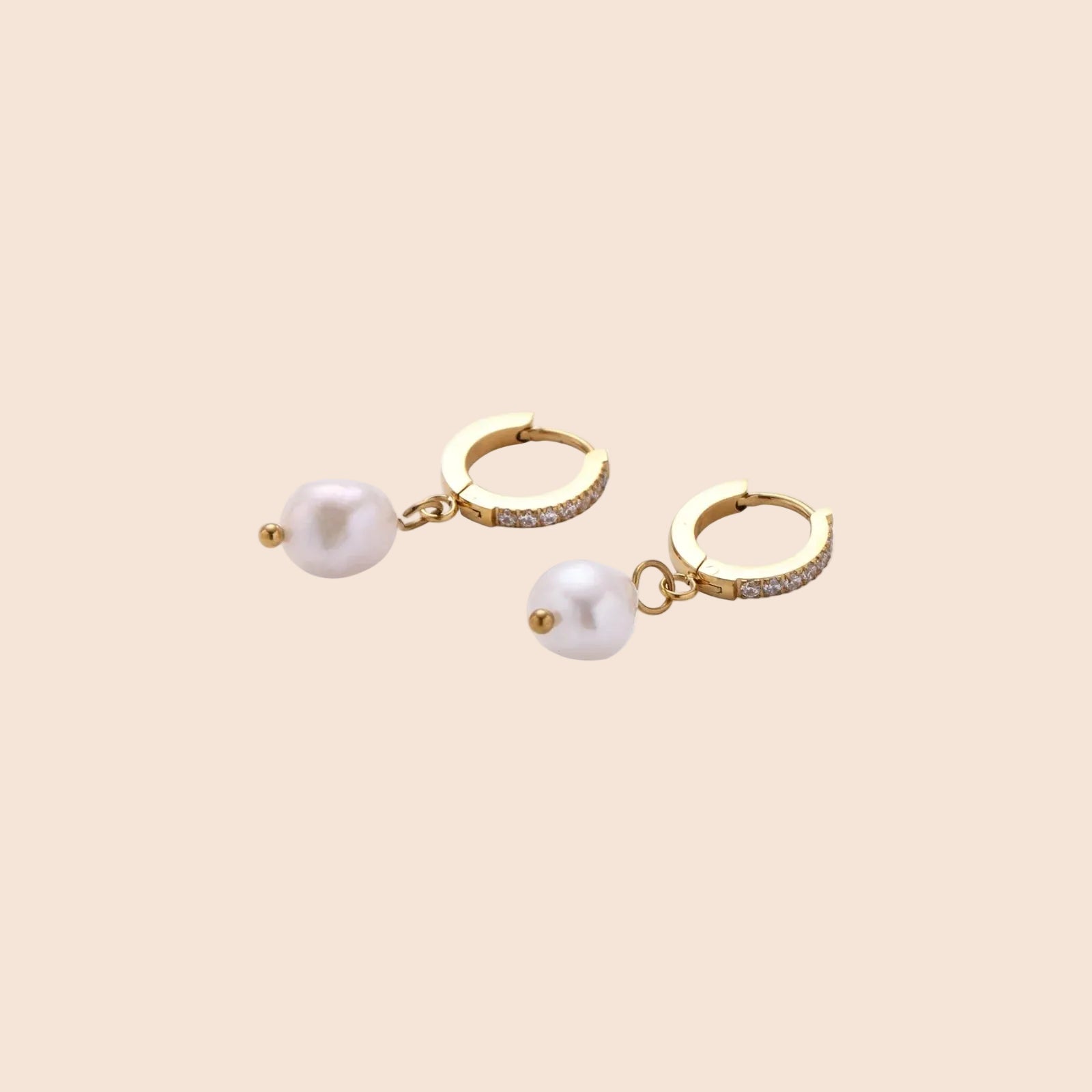 Gold huggie hoop earrings with pavé crystals and white freshwater pearl drops on cream background
