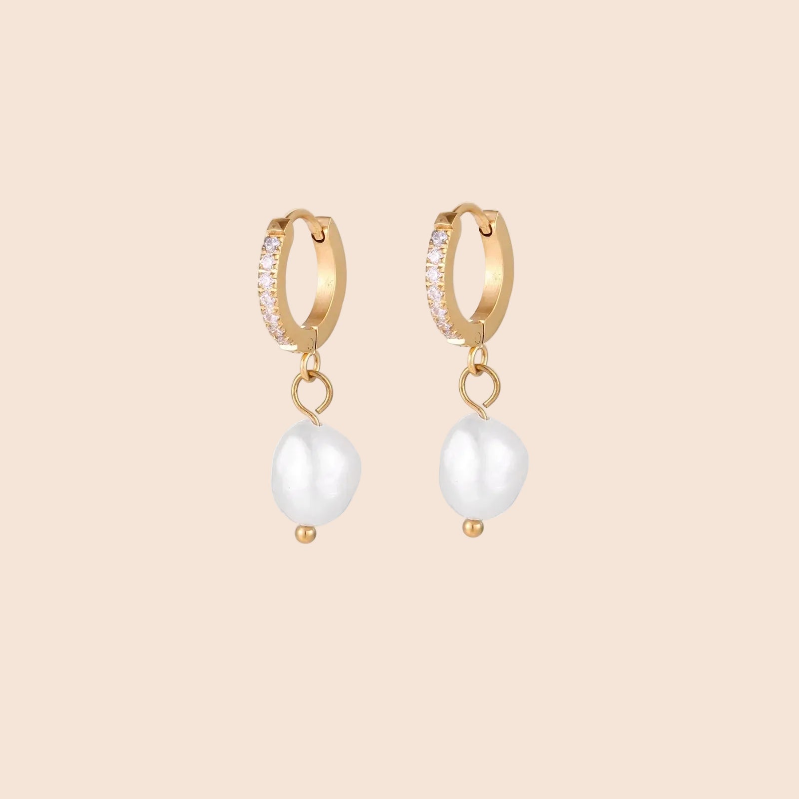 Gold huggie hoop earrings with pavé crystals and white freshwater pearl drops on cream background