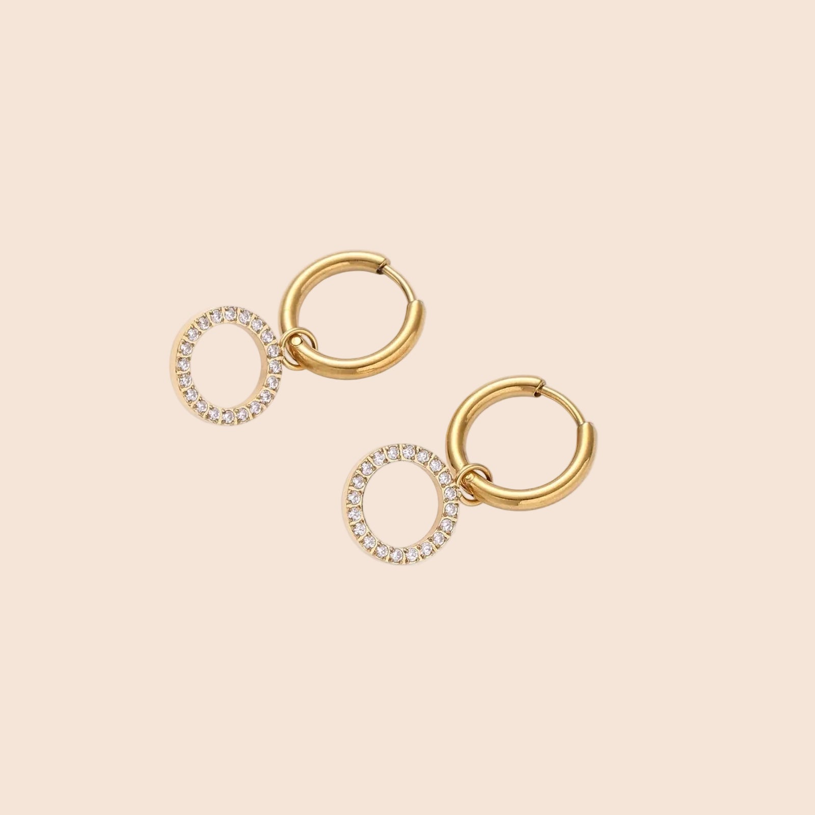 Gold-plated huggie hoop earrings with CZ-studded open circle charms on beige background