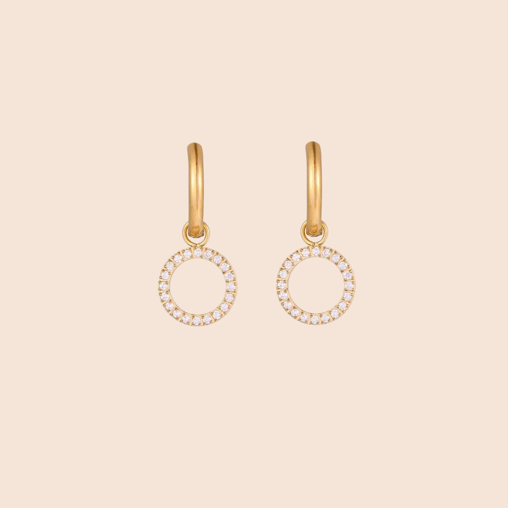 Gold-plated huggie hoop earrings with CZ-studded open circle charms on beige background