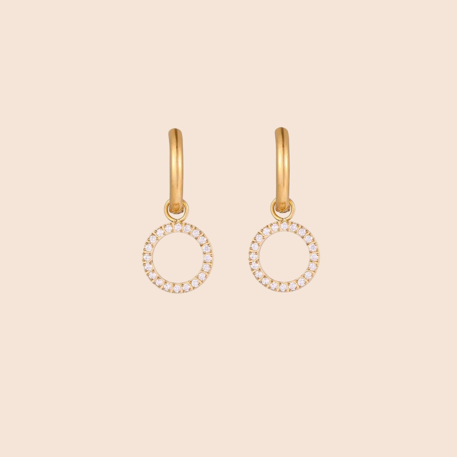 Gold-plated huggie hoop earrings with CZ-studded open circle charms on beige background