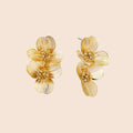 Pair of gold-plated double flower earrings with textured petals and crystal centers on cream background.