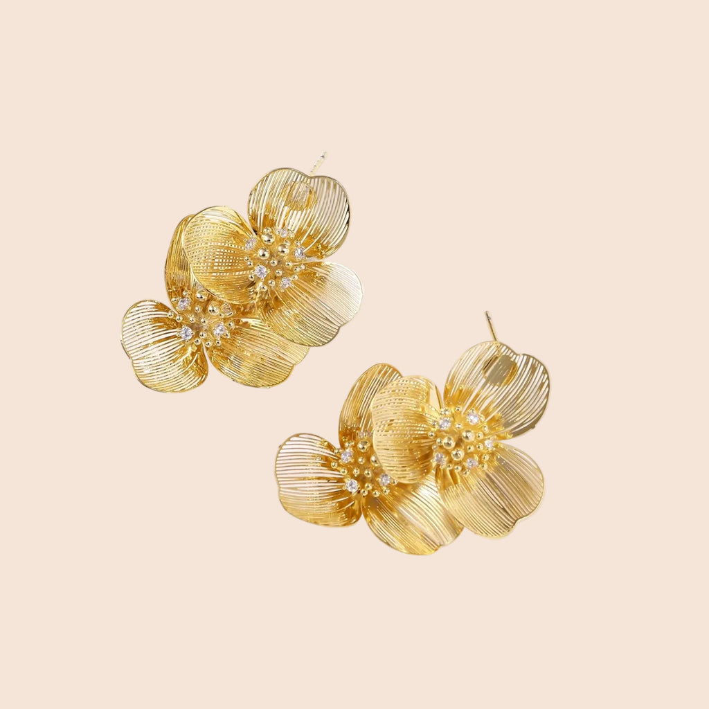 Pair of gold-plated double flower earrings with textured petals and crystal centers on cream background.