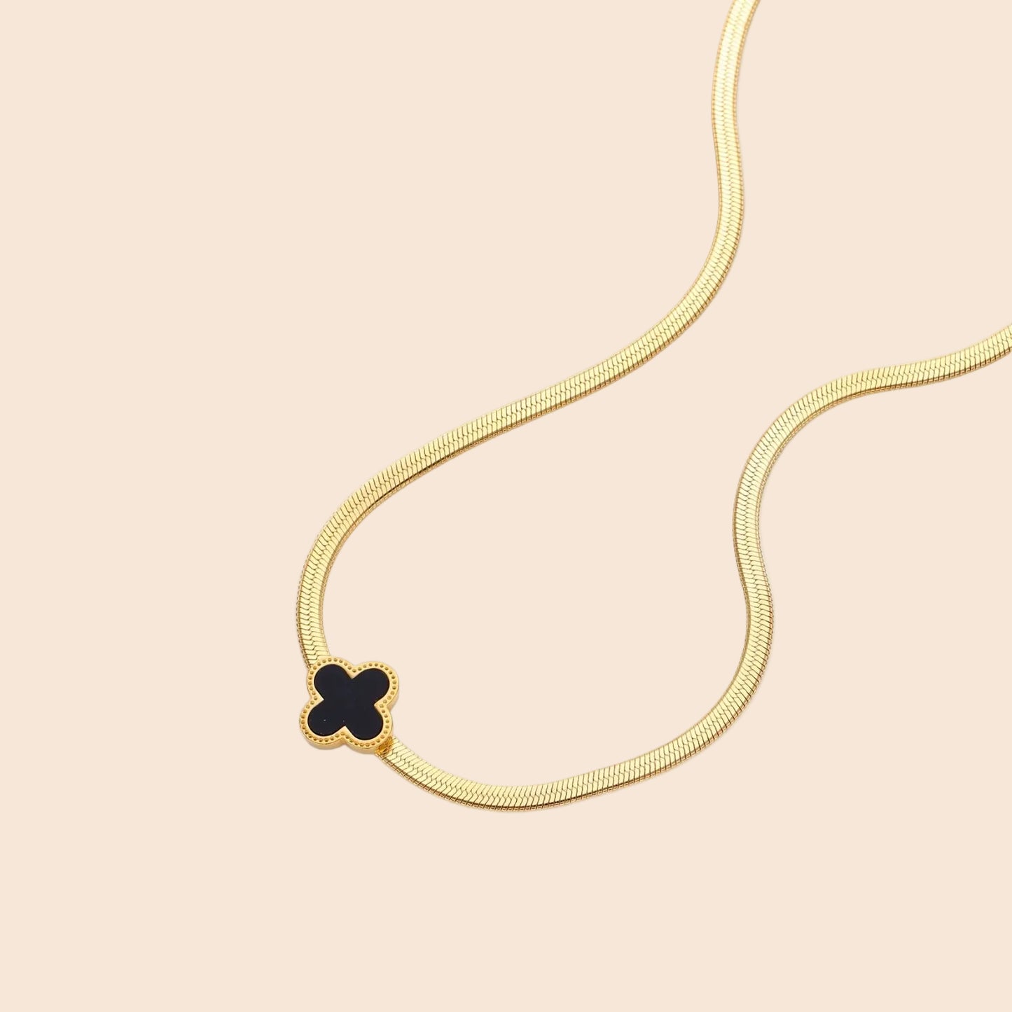 Dainty 18K gold-plated herringbone chain necklace with black enamel quatrefoil clover pendant on white background